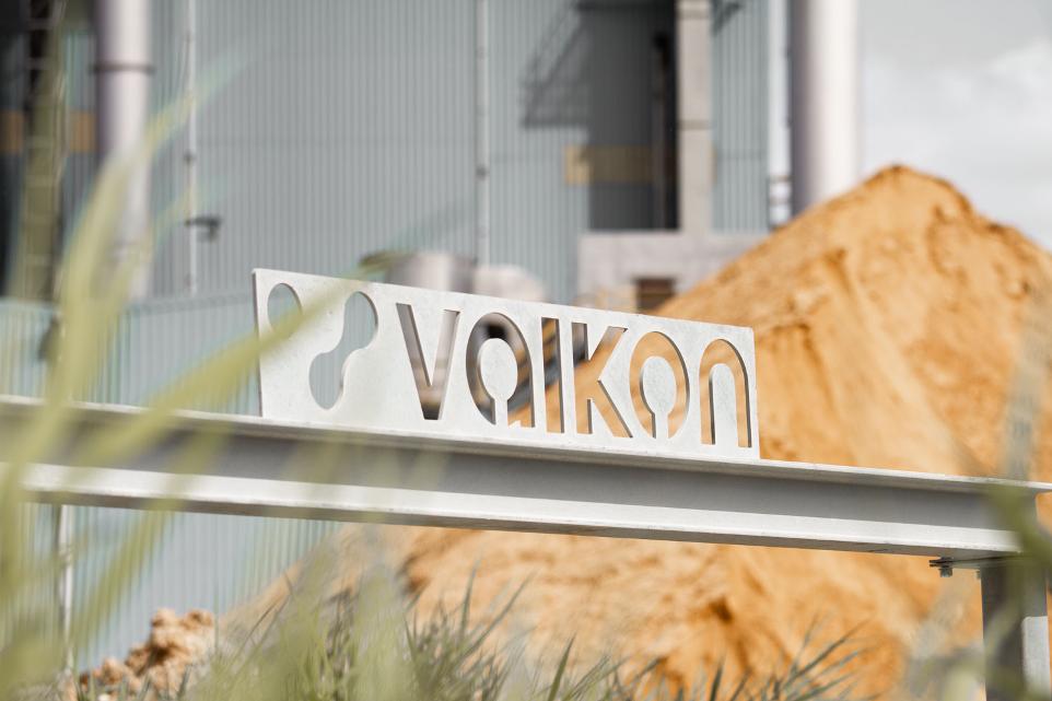 A metal construction with the Vaikon logo lasered inside. A sand processing factory is seen in the background.
